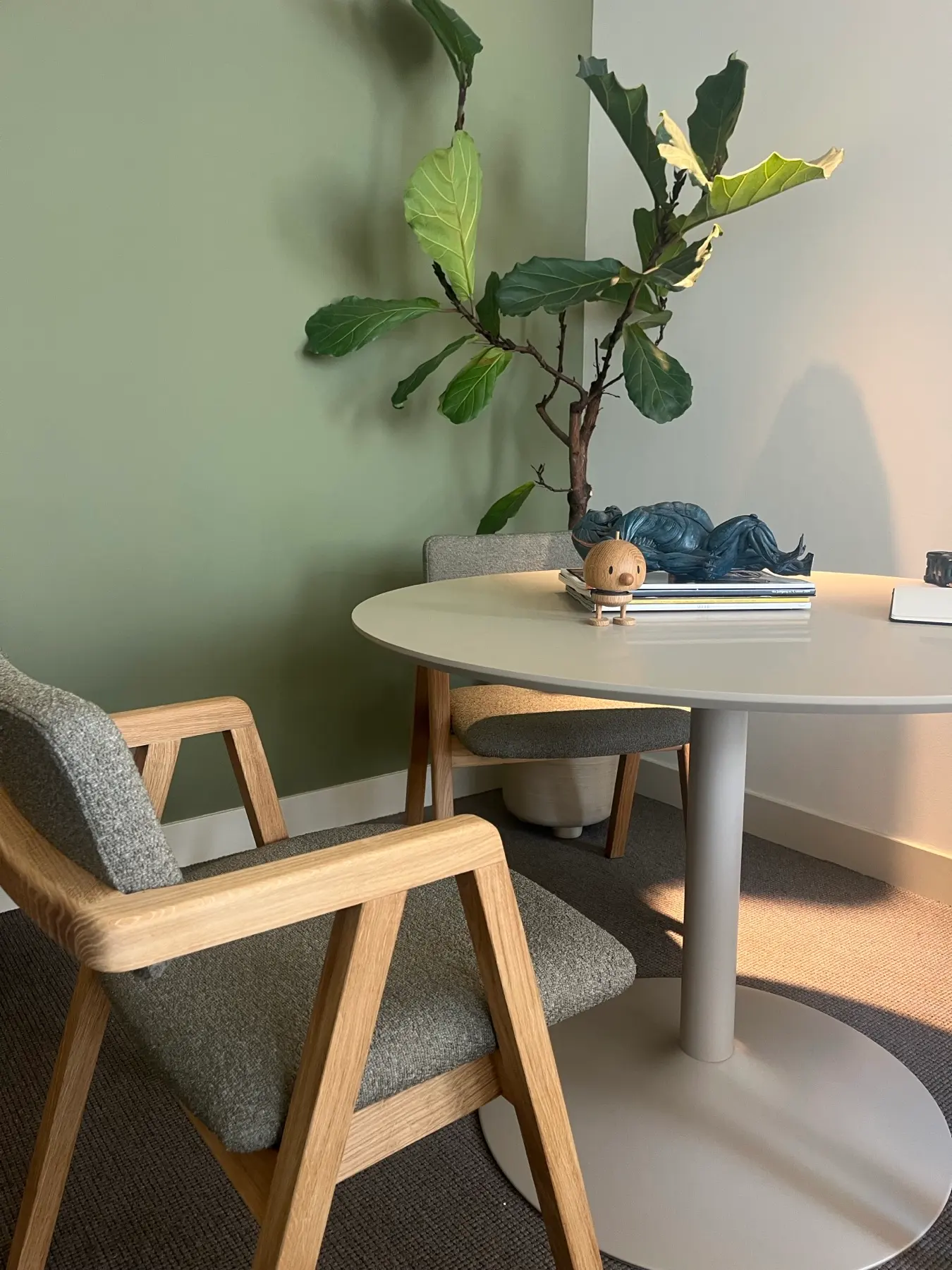 Overleghoek met saliegroene wand, ronde tafel en eiken stoelen